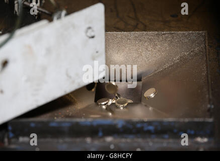 Unprägte 1-Pfund-Münzen fallen in eine Rutsche, um im Coin Press Room (CPR) in der Royal Mint in Pontyclun, Wales, geprägt zu werden.Sie werden zu den letzten Münzen, die vor einem Designwechsel 2016 in kreisförmiger Form produziert werden. Stockfoto