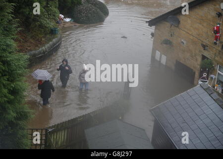 Die Menschen waten in Mytholmroyd in Calderdale, West Yorkshire, durch die Flutwässer, wo nach sintflutartigen Regengüssen die Hochwassersirenen erklangen. Stockfoto