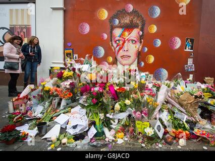 Die Menschen sehen Blumen, die an einem Wandgemälde des Musikers David Bowie in Brixton, im Süden Londons, nach der Ankündigung dieses Todes gestern zurückgelassen wurden. Stockfoto