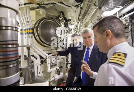 Verteidigungsminister Michael Fallon (Mitte) mit dem Konteradmiral der U-Boote und dem stellvertretenden Leiter des Marinestabs John Weale (links) und Daniel Martyn (rechts), der im Raketenabteil, in dem bis zu 16 Trident 2 D5-Atomraketen untergebracht werden können, den Kommandanten der HMS Vigilant anführt, Bei einem Besuch des U-Bootes HMS Vigilant der Vanguard-Klasse, eines der vier nuklearen U-Boote, die den Kriegskopf tragen, auf dem HM Naval Base Clyde, auch bekannt als Faslane, in Schottland. Stockfoto