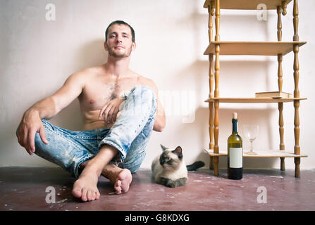 Porträt eines jungen Mannes sitzen auf dem Boden mit einer Katze und einer Flasche Wein Stockfoto