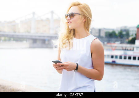 Lässige Frau mit Sonnenbrille mit blonden Haaren hält Smartphone Stockfoto