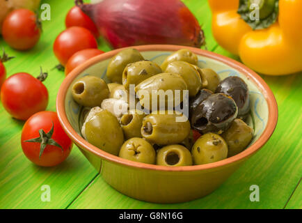 Grüne und schwarze Oliven und Gemüse am grünen Tisch Stockfoto