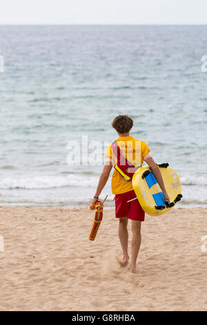 RNLI Rettungsschwimmer trägt im Juni Rettungsschlitten an Surfbretterausrüstung am Strand von Alum Chine, Bournemouth, Dorset UK Stockfoto