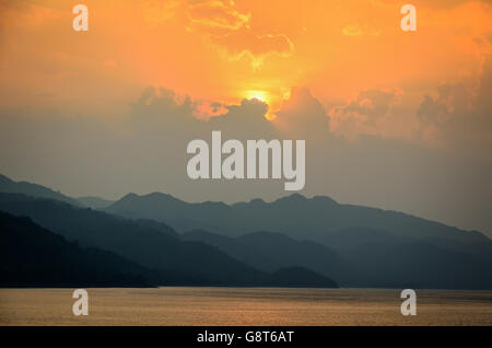 Schöne Landschaft während des Sonnenuntergangs über Bergketten am See in Srinakarin Damm, Provinz Kanchanaburi, Thailand Stockfoto