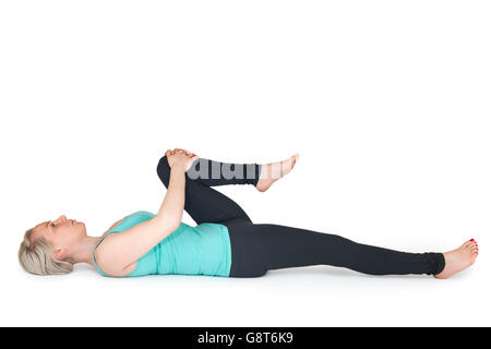 Körper-Gesamtansicht einer jungen blonden Frau in Yoga-Übung "in der Rückenlage, eine Knie mit den Händen zu gewinnen" gegen weiß Stockfoto