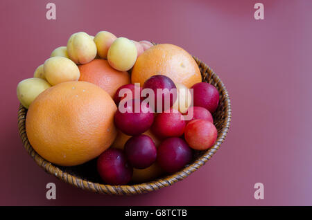 Weidenkorb Früchte wie Pflaumen, Orangen, Grapefruits und Aprikosen auf einander gestapelt Stockfoto