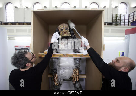 Arbeiter, die ein lebensgroßes Replikat des Predators handhaben, Das ist Teil der Installation The Personal Effects of Kim Dotcom (2013-) des Künstlers Simon Denny während einer Presseinterpremiere von emotional Supply Chain - einer Gruppenausstellung internationaler Künstler, "inspiriert von den digitalen Identitäten, die wir auf Plattformen wie Facebook und Instagram darstellen" - in der Zabludowicz Collection, London. Stockfoto