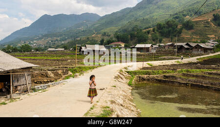 Kleine vietnamesische Mädchen allein zu Fuß in eine kleine Straße zwischen den Reisfeldern im Norden Vietnams Landschaft. Stockfoto