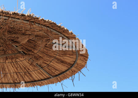 Strohgedeckten Sonnenschirm am strahlend blauen Himmelshintergrund Stockfoto