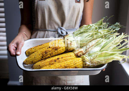 Eine Frau hält einen Teller voll mit frisch gegrilltem Mais, fotografiert aus der Vorderansicht. Stockfoto