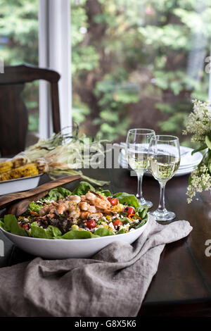 Eine große Schale mit gegrillten Shrimps und Feldsalat mit zwei Gläsern Weißwein begleitet werden fotografiert aus der Vorderansicht. Stockfoto