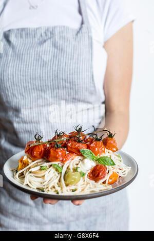Eine Frau hält einen Teller voll mit Caprese-Spaghetti mit gebratenen Tomaten, Basilikum und Mozzarella-Käse hergestellt. Stockfoto
