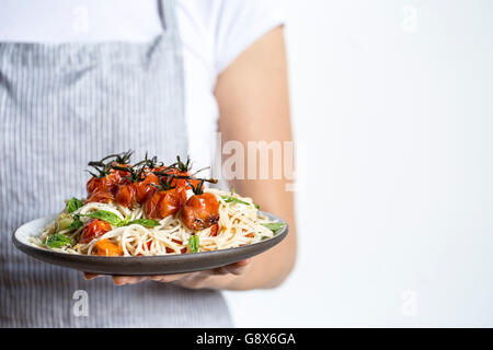 Eine Frau hält einen Teller voll mit Caprese-Spaghetti mit gebratenen Tomaten, Basilikum und Mozzarella-Käse hergestellt. Stockfoto