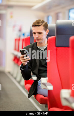 Glücklich Jüngling mit dem Zug reisen. Schreiben eine Nachricht auf Handy während der Fahrt mit dem Expresszug Tourist Stockfoto