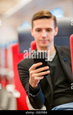 Glücklich Jüngling mit dem Zug reisen. Schreiben eine Nachricht auf Handy während der Fahrt mit dem Expresszug Tourist Stockfoto