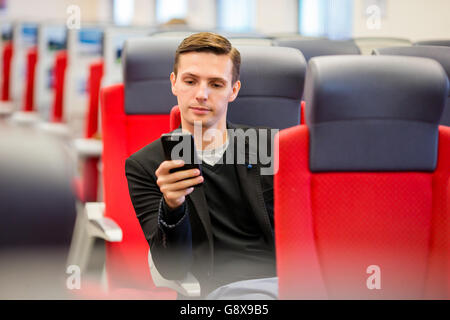 Junge Touristen Mann Reisen mit dem Zug. Schreiben eine Nachricht auf Handy während der Fahrt mit dem Expresszug Passagier Stockfoto