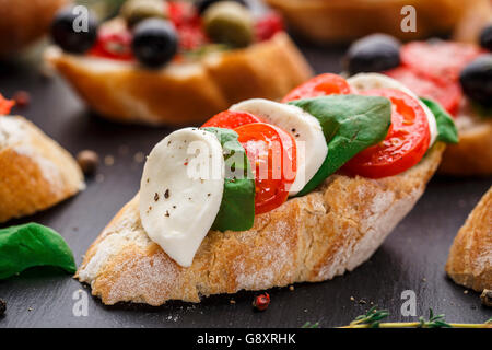 Italienische Bruschetta mit Tomaten, Mozzarella-Käse und Kräutern auf Schiefer Hintergrund Stockfoto