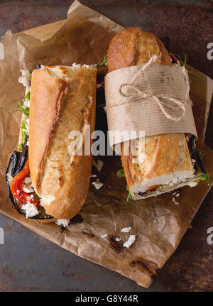 Zwei Hälfte vegetarische Baguette u-Boot-Sandwich mit gegrillter Aubergine, Paprika und Feta Käse auf Backpapier Papier über dunkle Rusty Stockfoto