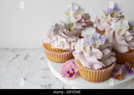 Lila Cupcakes mit gezuckerten essbare Blumen auf Kuchen Stand Kopie Raum Hintergrund Stockfoto