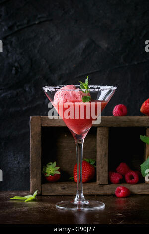 Cocktailglas Erdbeer Dessert mit Sorbet, serviert auf dunklem Hintergrund mit Erdbeeren, Himbeeren und Minze Behi gezuckert Stockfoto