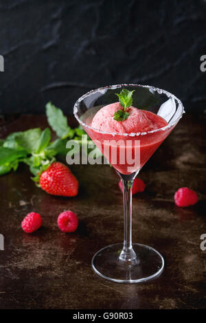 Cocktailglas Erdbeer Dessert mit Sorbet, serviert auf dunklem Hintergrund mit Erdbeeren, Himbeeren und Minze Behi gezuckert Stockfoto