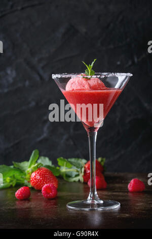 Cocktailglas Erdbeer Dessert mit Sorbet, serviert auf dunklem Hintergrund mit Erdbeeren, Himbeeren und Minze Behi gezuckert Stockfoto
