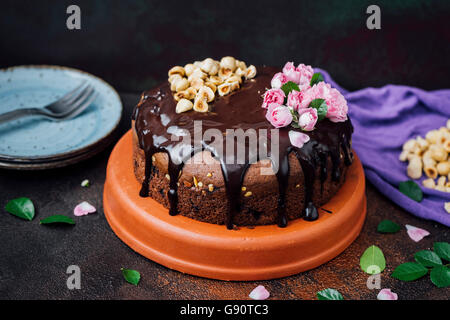 Haselnuss-Schokoladen-Kuchen mit Schokoladenganache bedeckt und mit Haselnüssen und rosa Rosen dekoriert. Stockfoto