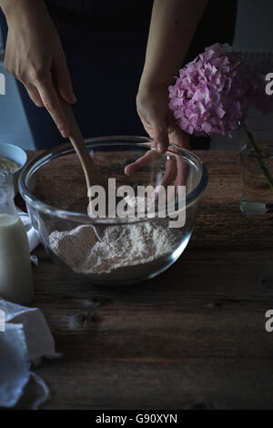 Mischen Mehl mit einem Holzlöffel in einer Schüssel auf einem rustikalen Holztisch Hände Stockfoto