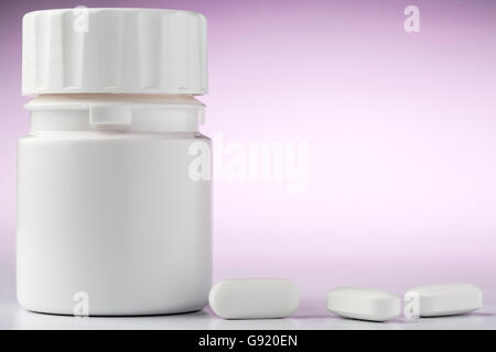 Eine Flasche Aspirin-Tabletten und drei Pillen im Vordergrund. Close-up auf rosa Hintergrund Stockfoto