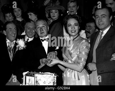 Unterstützt von Julie Andrews, die in der Show Eliza Doolittle spielt, wird Mr. Austin Melford bei der traditionellen zwölften Abendzeremonie den Baddeley-Kuchen für Mitglieder der Besetzung des amerikanischen Musicals schneiden sehen. Links, mit Knopfloch, ist Stanley Holloway, Star der Show. Stockfoto