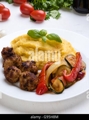 Polenta mit Frikadellen und gebratenem Gemüse auf einem weißen Teller Stockfoto