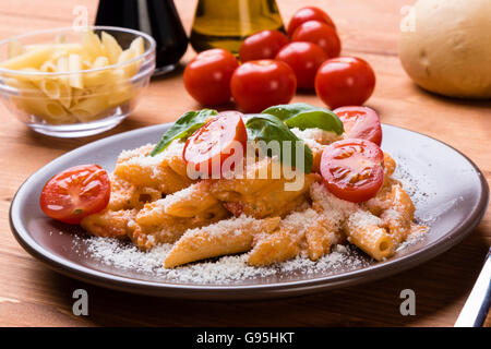 Penne mit Tomaten-Basilikum und Käse in braun Platte auf Holztisch Stockfoto