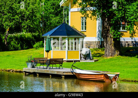 Bjornavad, Schweden – 20. Juni 2016: Kleine orangenes Ruderboot neben einem hölzernen Steg festgemacht. Gelben Pavillon am Rasen hinter sich. Outdoor-f Stockfoto