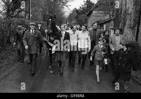 Bibliotheksdatei des Gewinners der Grand National Steeplechase Highland Wedding, der einen Helden durch Fyfield, Hampshire, nach seiner Rückkehr in den Stall von Trainer Toby Balding (mit Brille, rechts) nach seinem Triumph bei Aintree mit Jockey Eddie Harty, der Hand auf dem Pferd hat, voranbringen konnte. Stockfoto