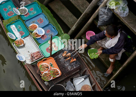 Frau grillt Fisch auf einem Longtail-Boot, für Touristen am Fluss Maeklong in Thailand zu dienen. Stockfoto