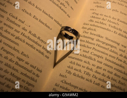 Ring wirft einen herzförmigen Schatten in Buch. Stockfoto