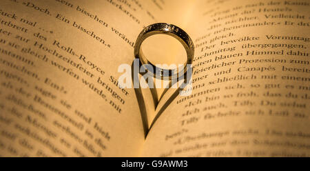 Ring wirft einen herzförmigen Schatten in Buch. Stockfoto