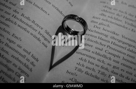 Ring wirft einen herzförmigen Schatten in Buch. Stockfoto
