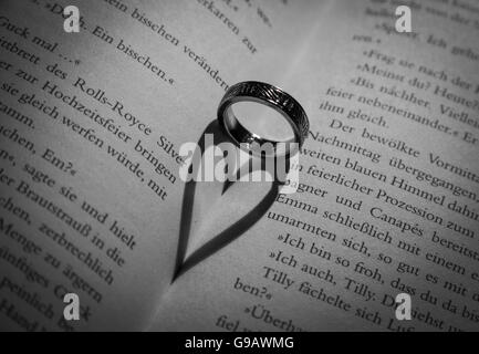 Ring wirft einen herzförmigen Schatten in Buch. Stockfoto