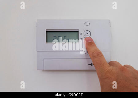 Mann, Anpassung nach Hause Zentralheizung Thermostat um Temperatur zu senken und Energie und Geld sparen. Stockfoto