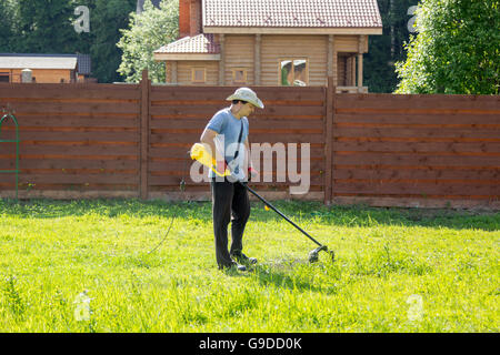 Mann mäht den Rasen mit einem Rasentrimmer Stockfoto