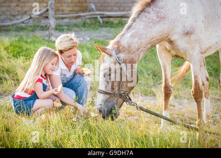 Mutter und Tochter, die Fütterung eines Pferdes eines Apfels im Gestüt. Stockfoto