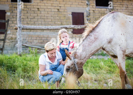 Mutter und Tochter, die Fütterung eines Pferdes eines Apfels im Gestüt. Stockfoto