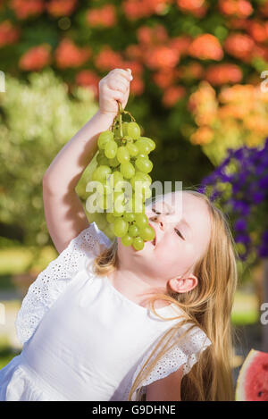 Schöne glückliche kleine Mädchen essen leckere grüne Trauben. Stockfoto