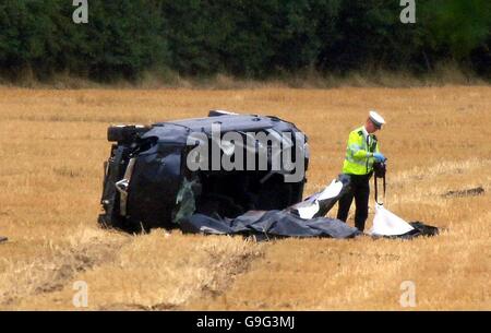 Ein Polizeibeamter inspiziert einen Personenkräger, der auf seiner Seite auf einem Feld nahe der Kreuzung 29 der Autobahn M25 liegt, nachdem der Wagen heute Morgen abgestürzt ist. Drei Personen wurden am Tatort für tot erklärt. Stockfoto