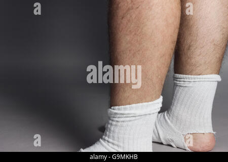 stehende Füße mit weißen Socken und ein großes Loch vor grauem Hintergrund Stockfoto