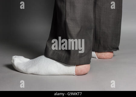 seitlich stehen Füße mit weißen Socken und ein großes Loch vor grauem Hintergrund Stockfoto