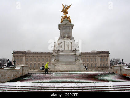 Ein Mann schaufelt Schnee von den Stufen vor der Statue von Queen Victoria, außerhalb des Buckingham Palace im Zentrum von London. Stockfoto