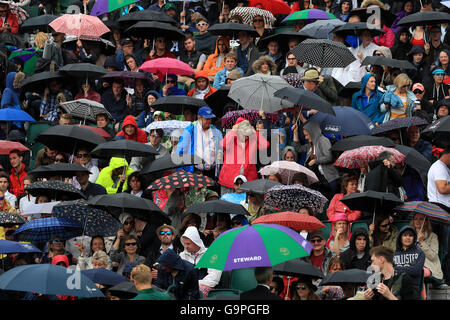 Regenschirme gehen in der Masse wie Regen am Tag fünf der Wimbledon Championships bei den All England Lawn Tennis and Croquet Club, Wimbledon fällt. Stockfoto